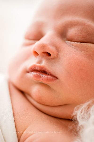 A close-up of a sleeping newborn baby with closed eyes and slightly parted lips, wrapped in a soft white blanket. Perfect for newborn photography without props, the baby’s peaceful face fills the frame.