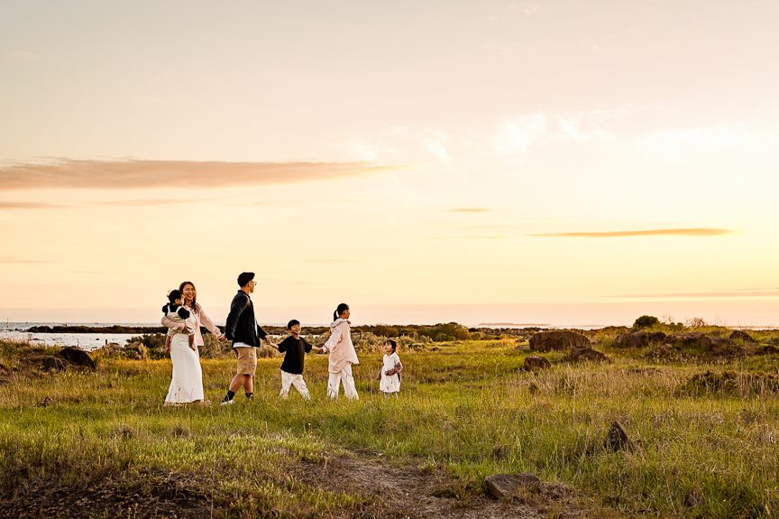 A family of six, including two adults and four children, walks together through a grassy field at sunset—a warm, peaceful moment that highlights one of the best photography session locations. The sky is mostly clear with a few gentle clouds overhead.