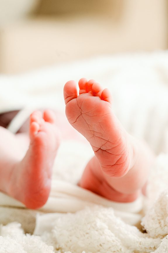Close-up of a baby's feet lying on a soft, white blanket. The tiny, pink soles radiate innocence and warmth—a tender moment beautifully captured by a Family and Newborn Photographer Melbourne West