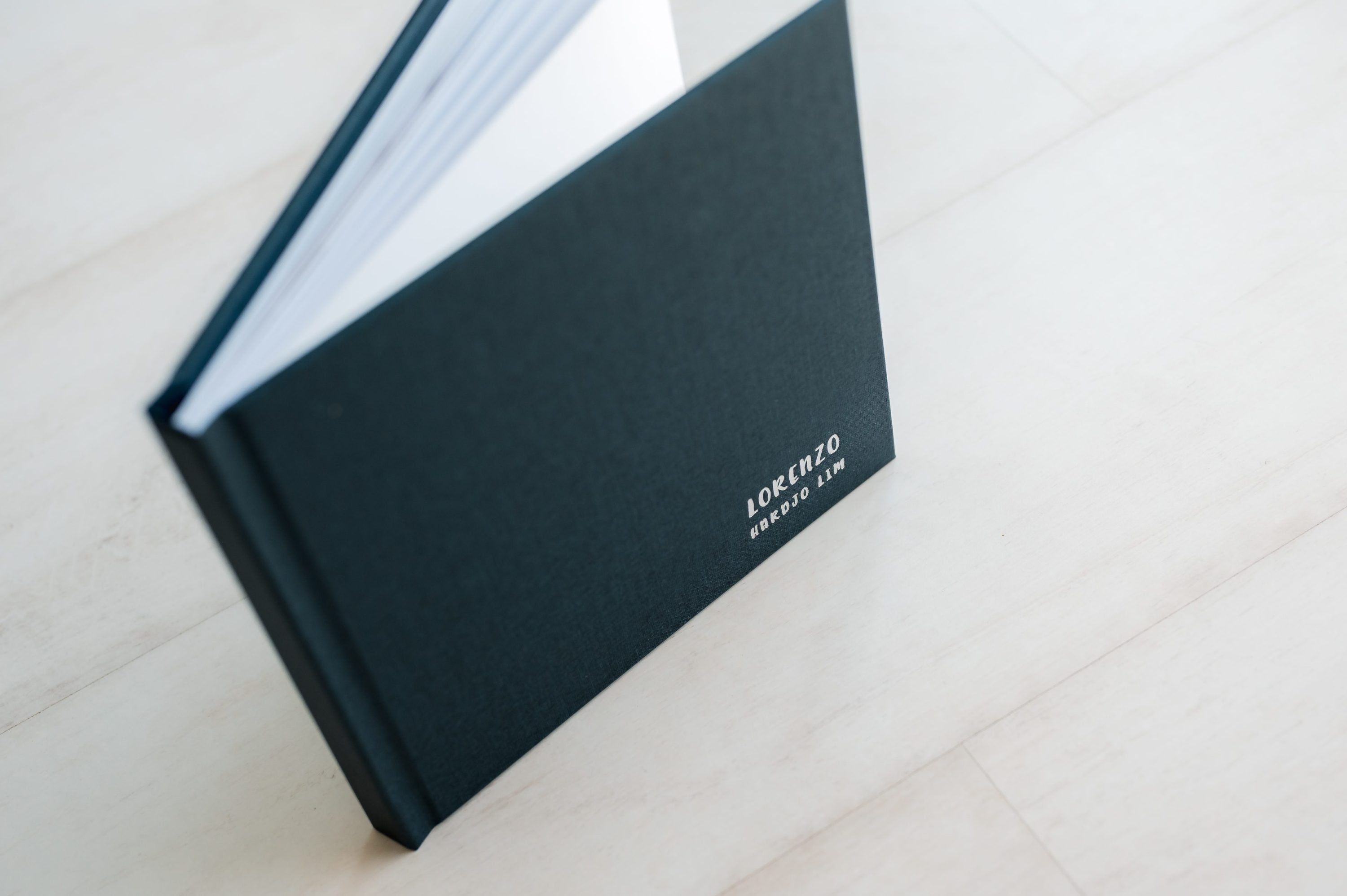 A dark green heirloom album standing upright on a light-coloured wooden surface, partially open with some pages visible—perfect for preserving treasured newborn photography Melbourne moments.