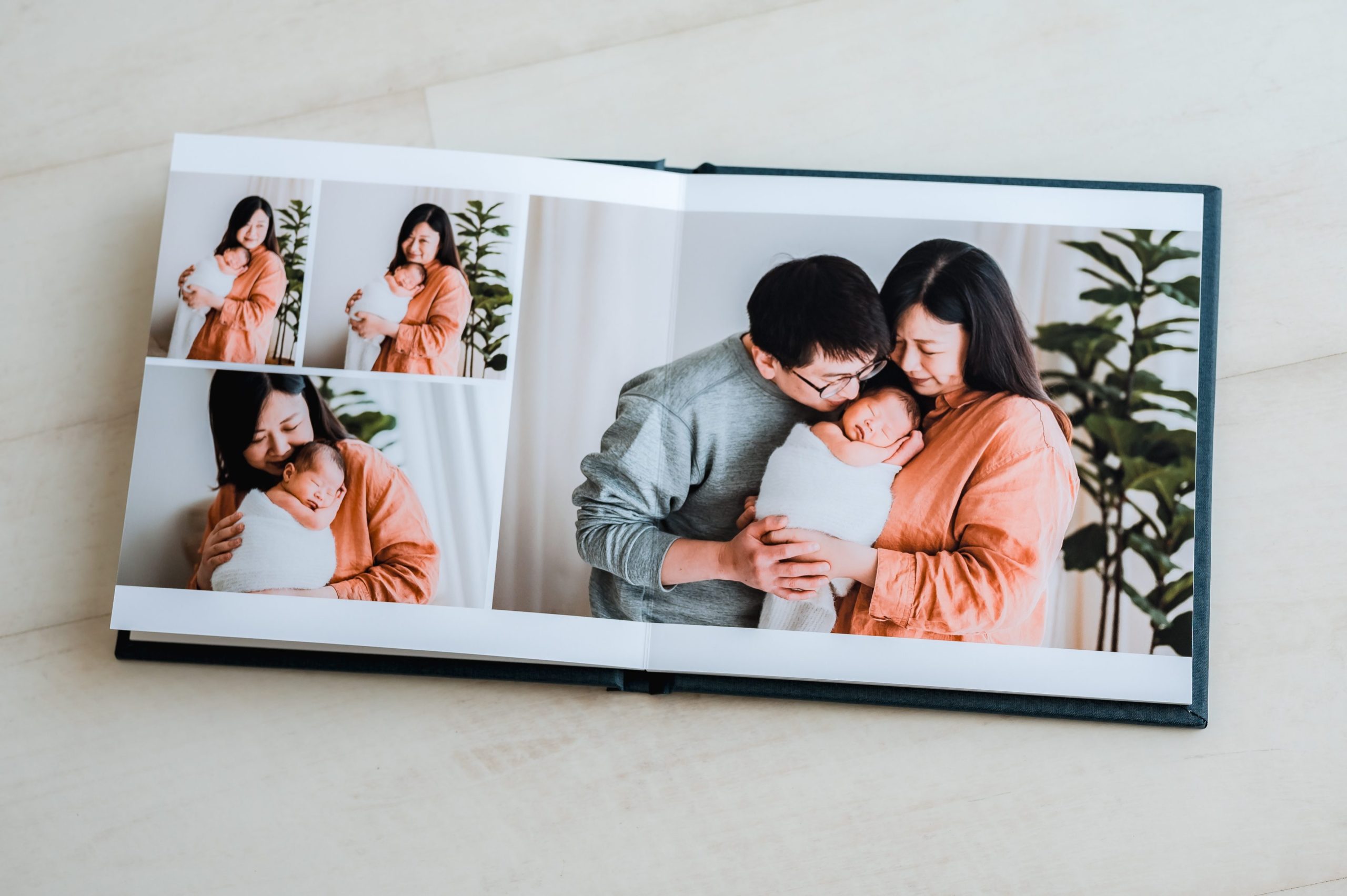 An open heirloom album displays pictures of a couple holding a newborn, smiling and embracing the baby while standing near a plant in a bright room—perfect for showcasing newborn photography Melbourne moments.