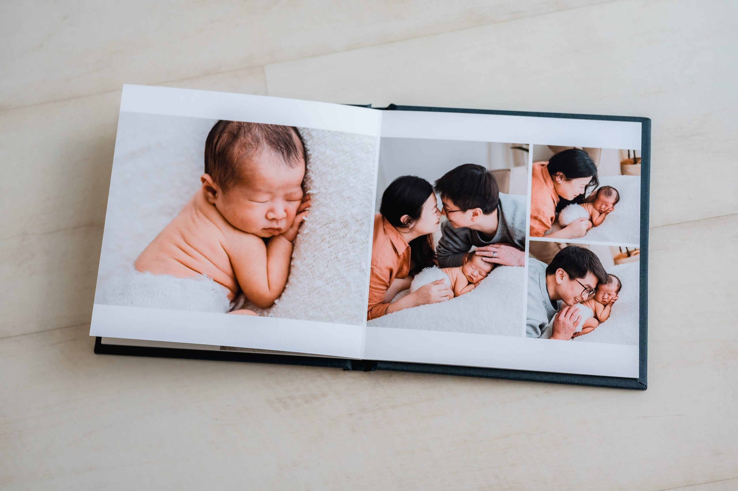 An heirloom album displays pictures of a newborn baby sleeping and a couple cuddling and kissing the baby, capturing tender family moments on a light wooden surface—perfect for those seeking timeless newborn photography Melbourne treasures.