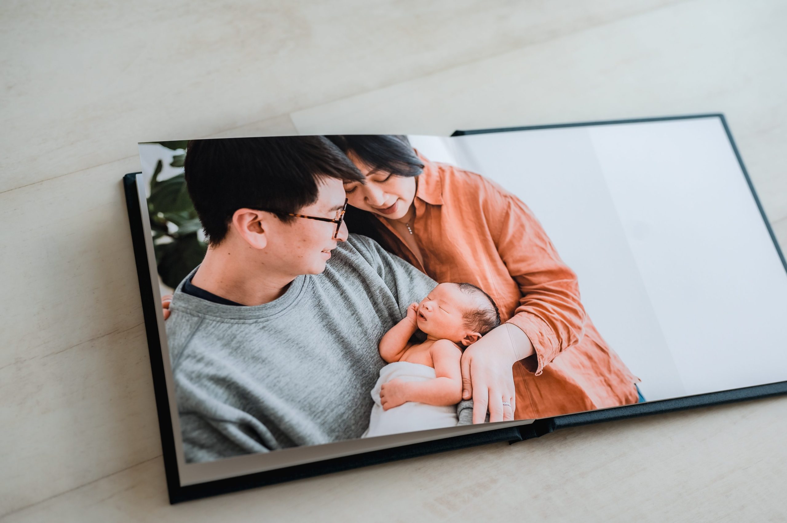 An open heirloom album displays a picture of a smiling couple gently holding a newborn baby, capturing a warm and tender family moment with timeless newborn photography Melbourne style.