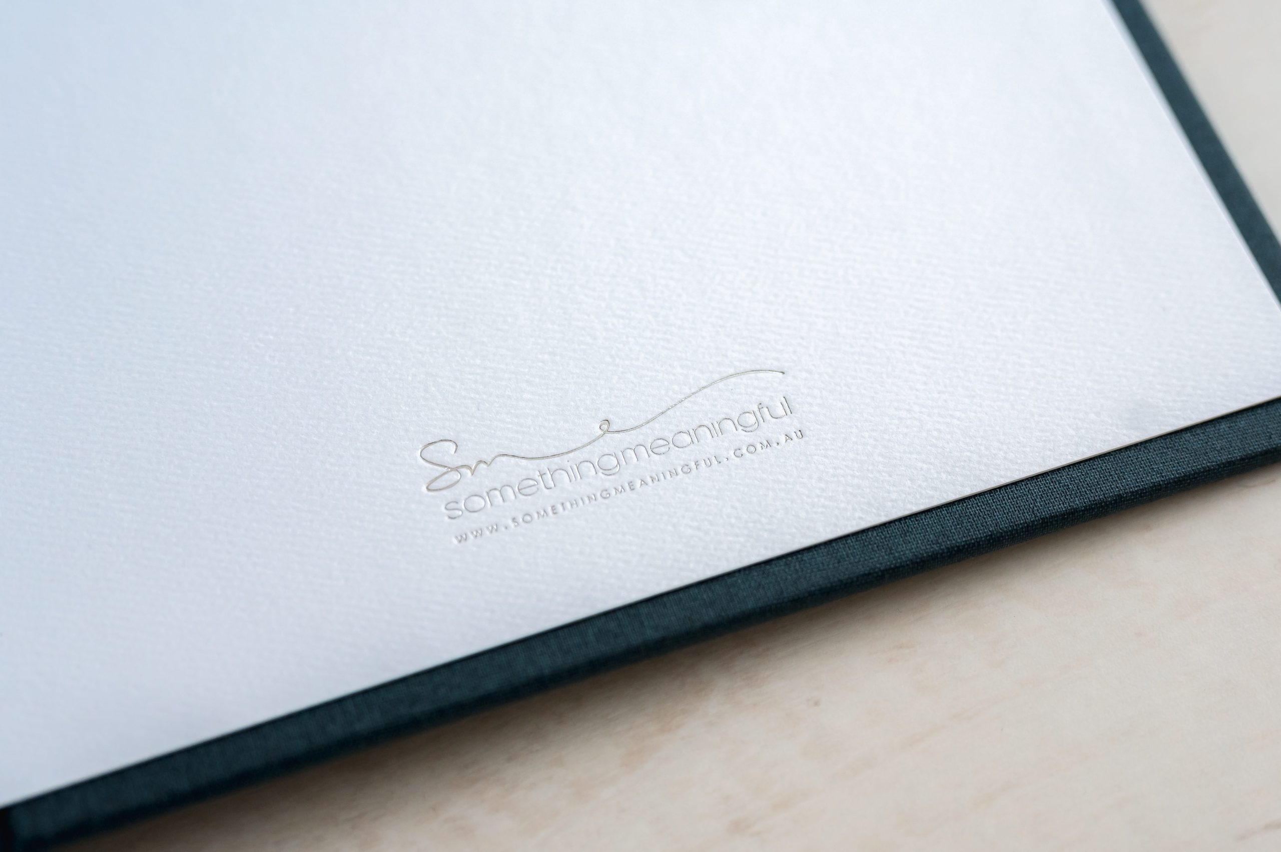 A close-up of a white textured paper with the words something meaningful and a website printed in small, elegant font near the bottom right corner—perfect for an heirloom album or showcasing newborn photography Melbourne. The edge of a dark cover is visible along the right side.