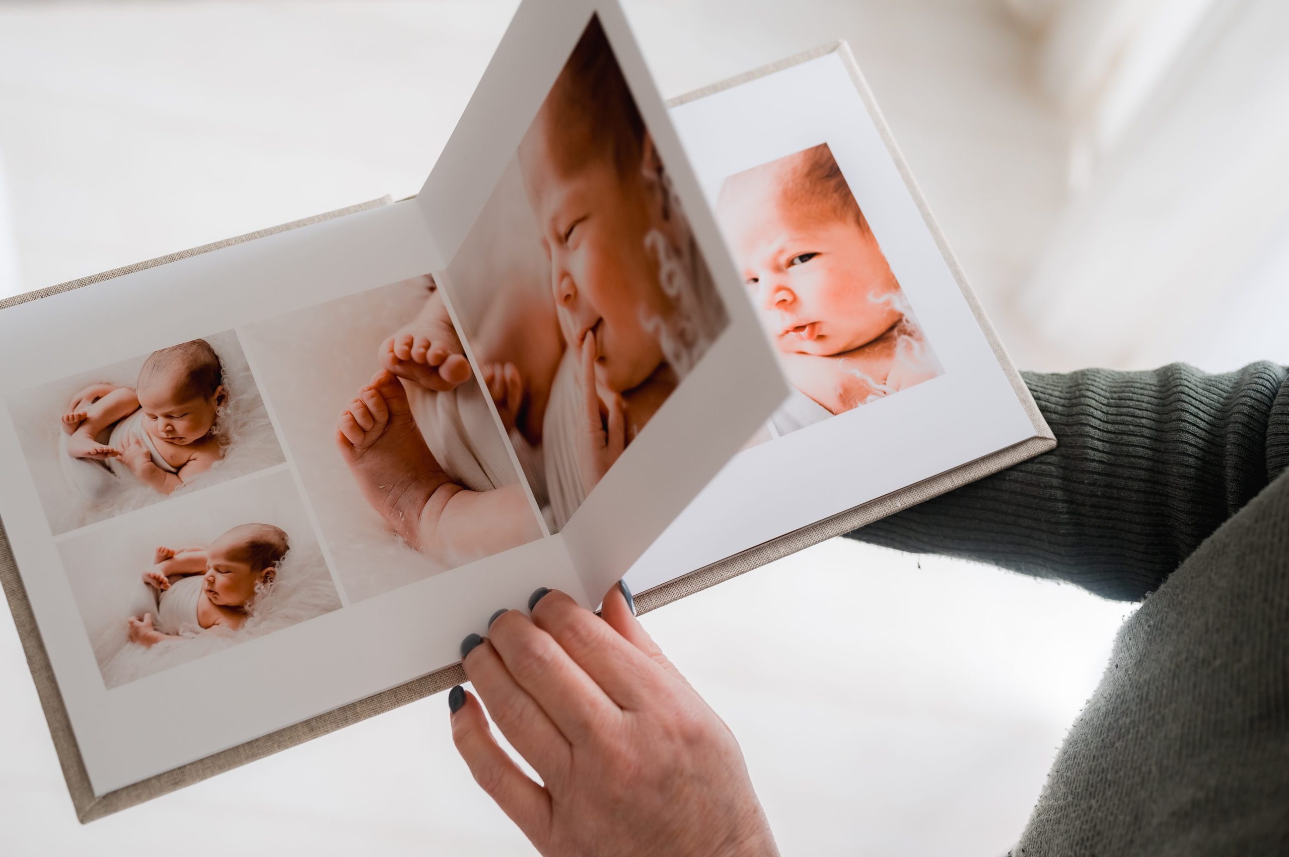 A person holding and flipping through a beautiful heirloom album featuring close-up pictures of a newborn baby, including the baby's face, hands, and feet—capturing precious moments of newborn photography Melbourne.