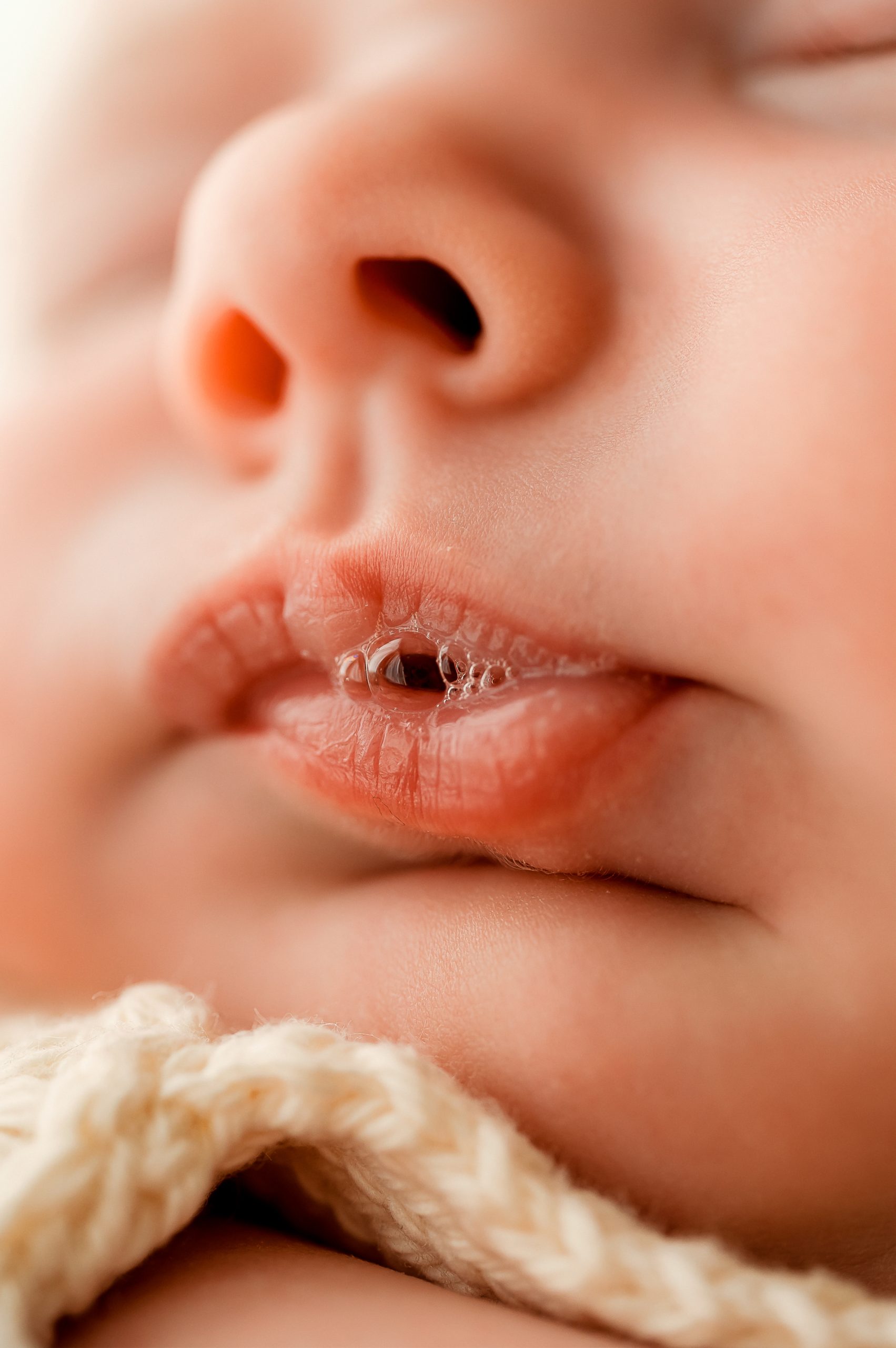 Close-up of a baby’s face, focusing on the lips with tiny bubbles of saliva. The baby’s skin appears soft, and a knitted cream-colored blanket is partially visible—perfect for newborn photography Melbourne style.